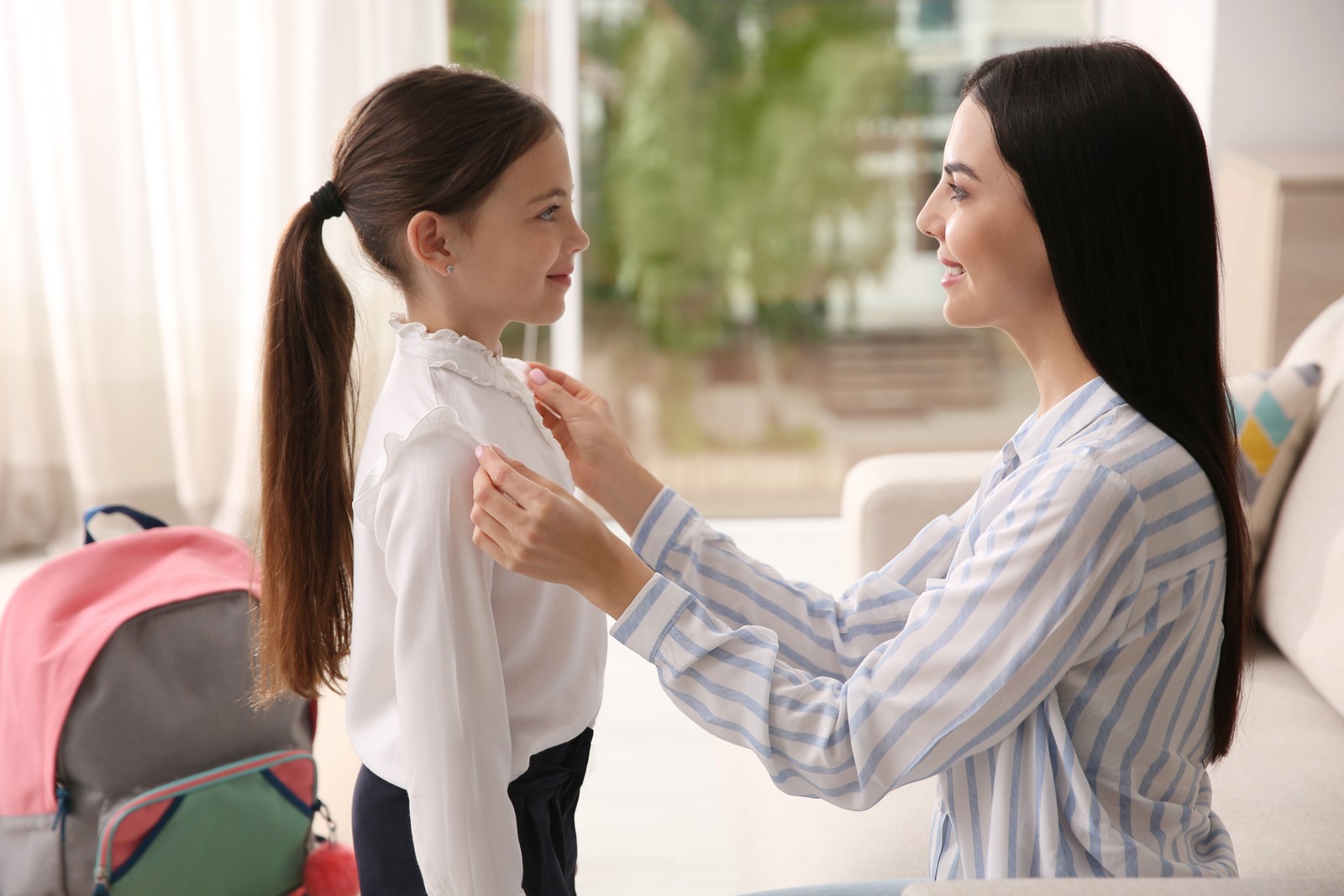 Photo of mother helping her little daughter to get ready for school indoors