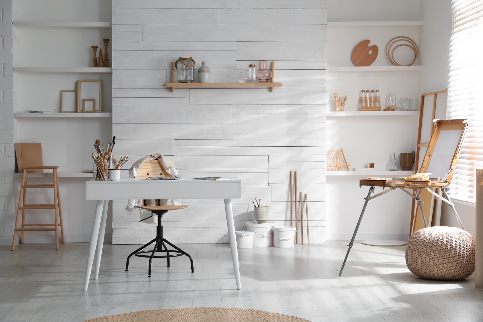 Photo of modern studio interior with artist's workplace and wooden easel near large window