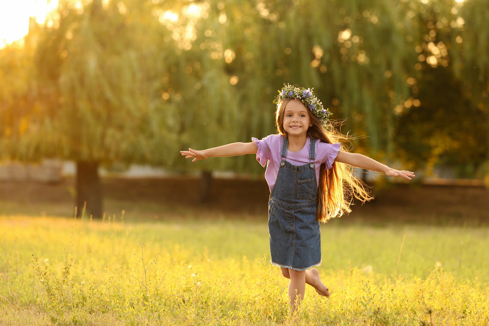 Photo of cute little girl wearing flower wreath outdoors at sunset, space for text. Child spending time in nature