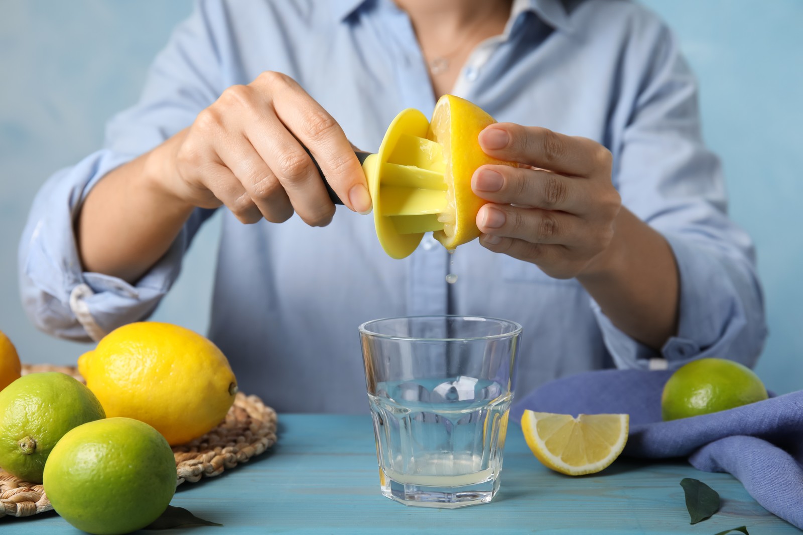 Photo of woman squeezing lemon juice with citrus reamer at light blue wooden table, closeup