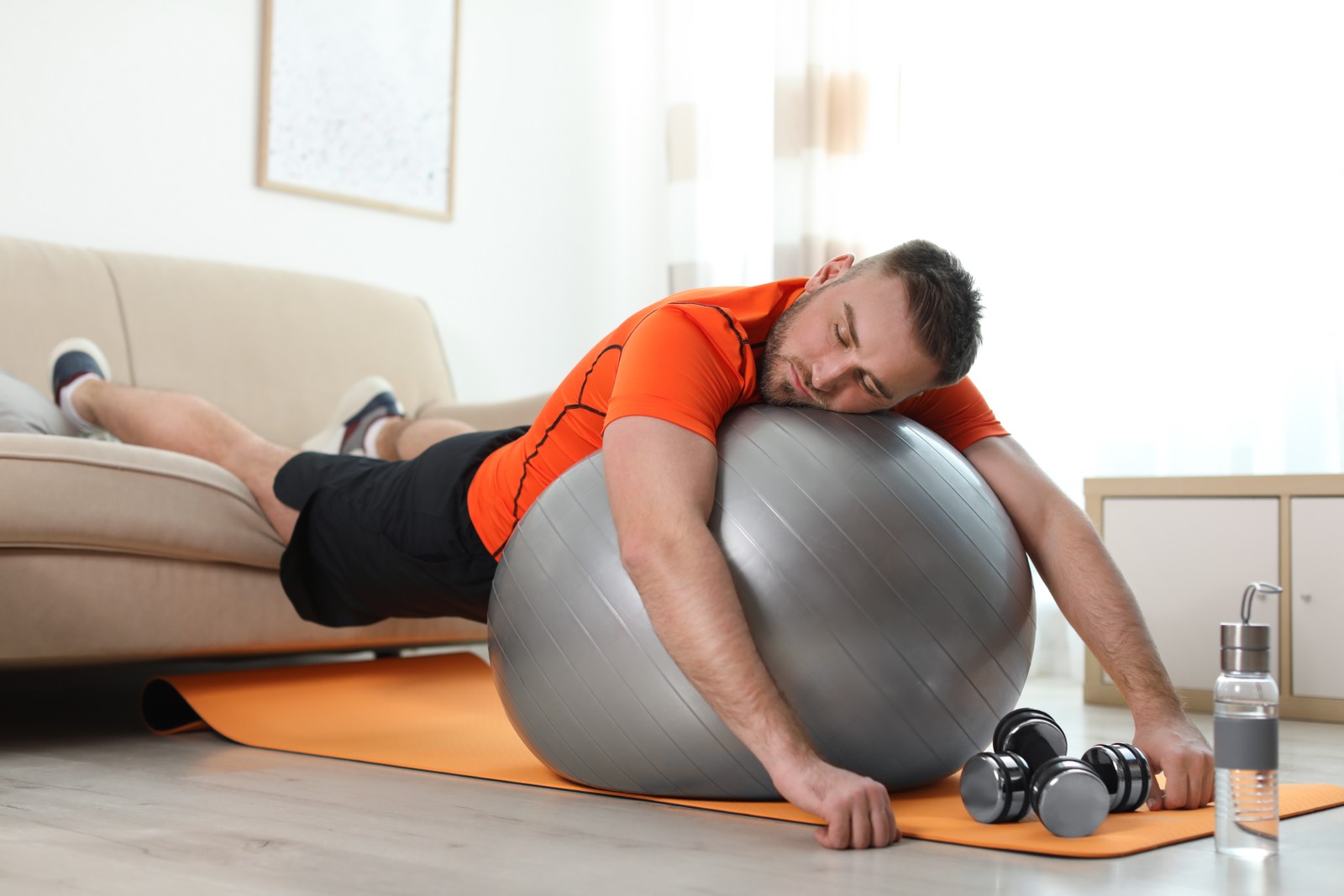 Photo of lazy young man with sport equipment at home