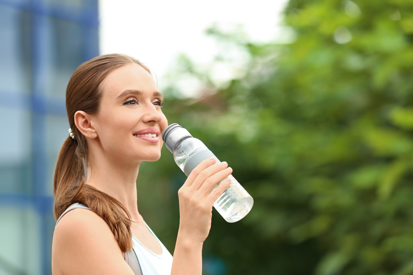Photo of young woman with bottle of water outdoors. Refreshing drink