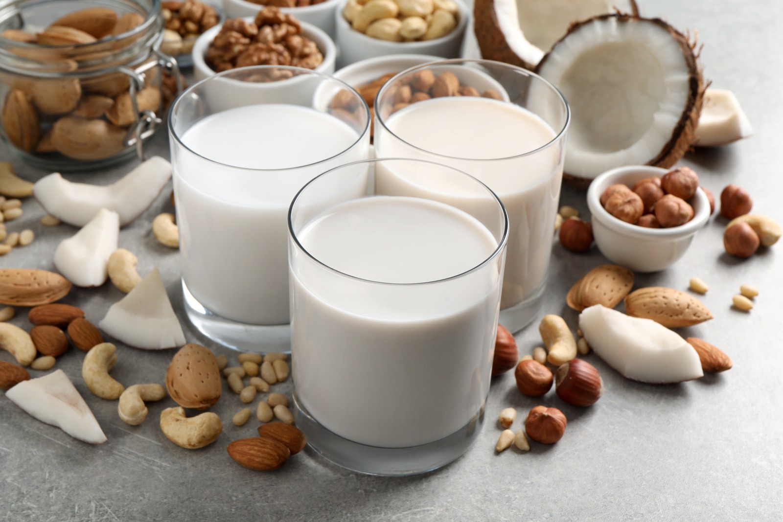 Photo of vegan milk and different nuts on grey table