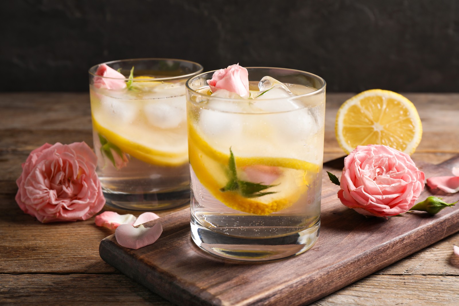 Photo of delicious refreshing drink with lemon and roses on wooden table