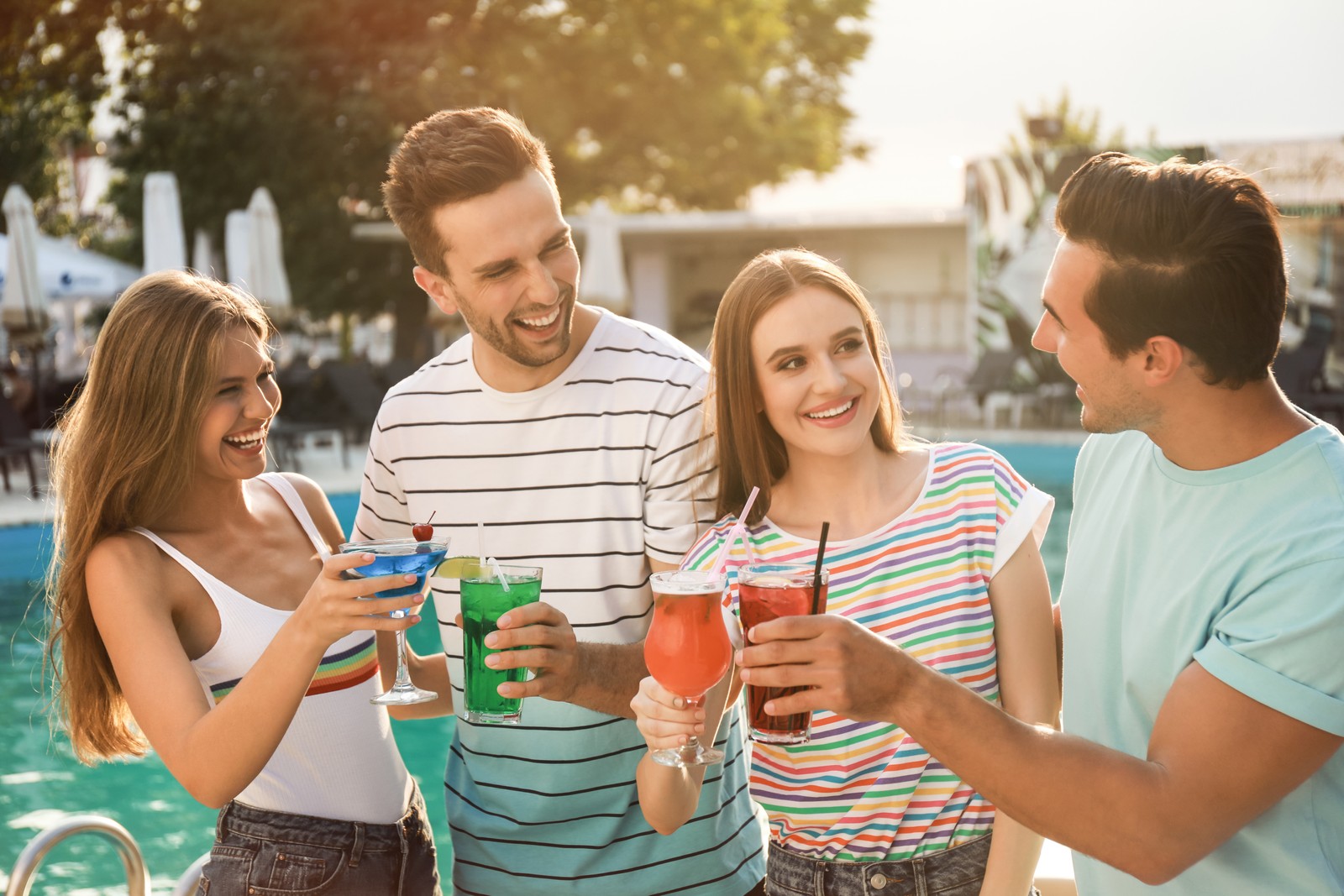 Photo of happy young friends with fresh summer cocktails relaxing near swimming pool