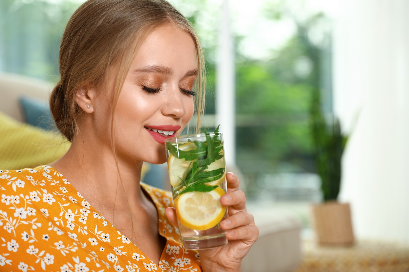 Photo of young woman with glass of lemonade at home. Refreshing drink