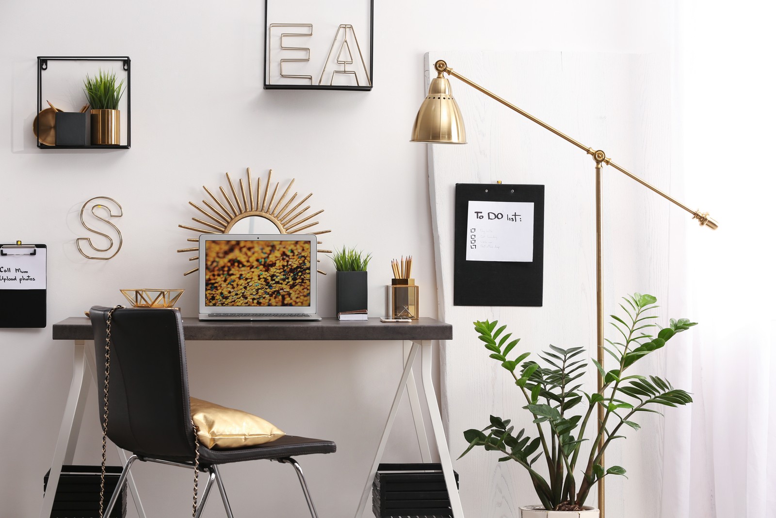 Photo of modern workplace with laptop and golden decor on desk near wall. Stylish interior design