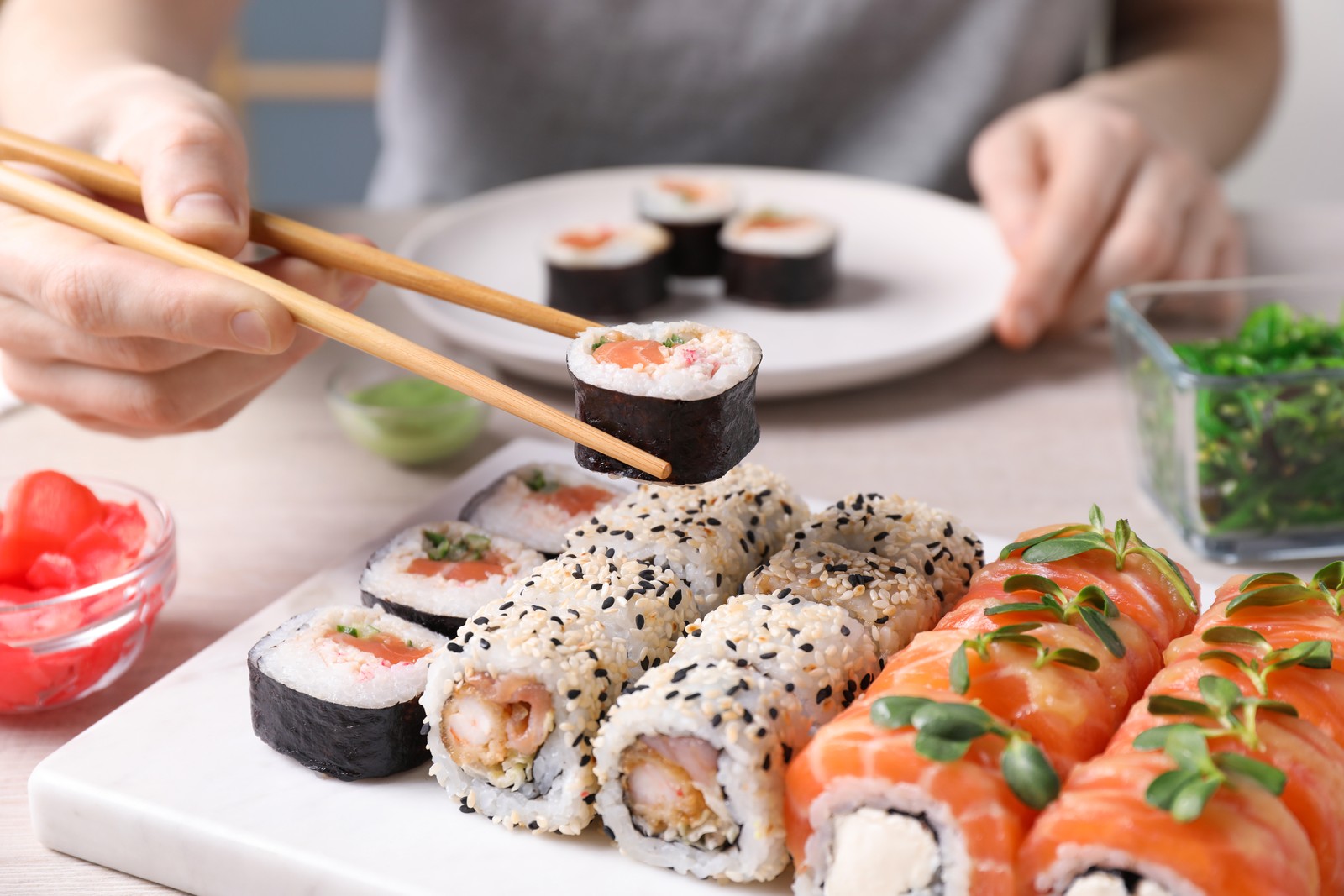 Photo of woman taking tasty sushi roll with salmon from set at table, closeup