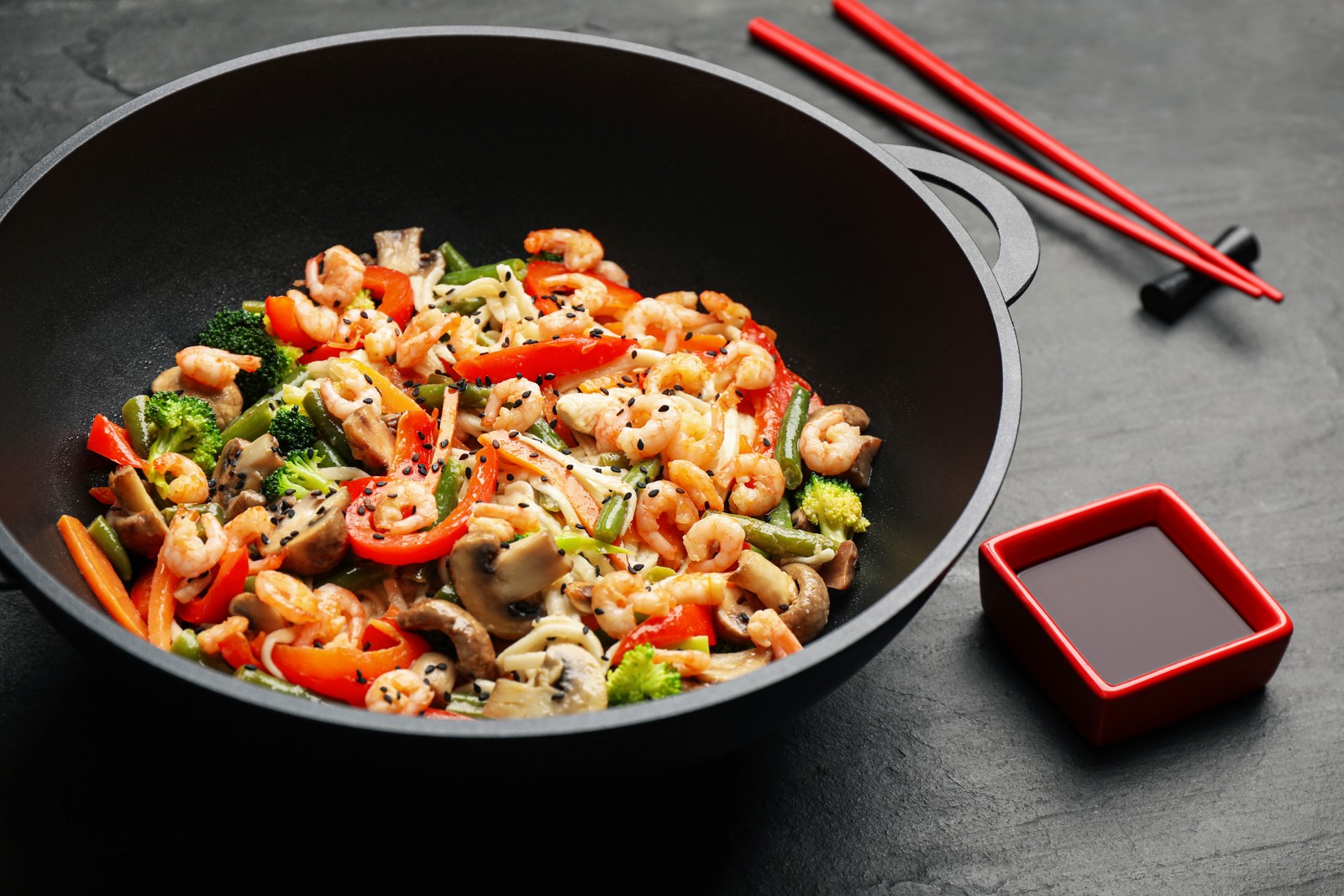 Photo of stir fried noodles with mushrooms, shrimps and vegetables in wok on black table, closeup