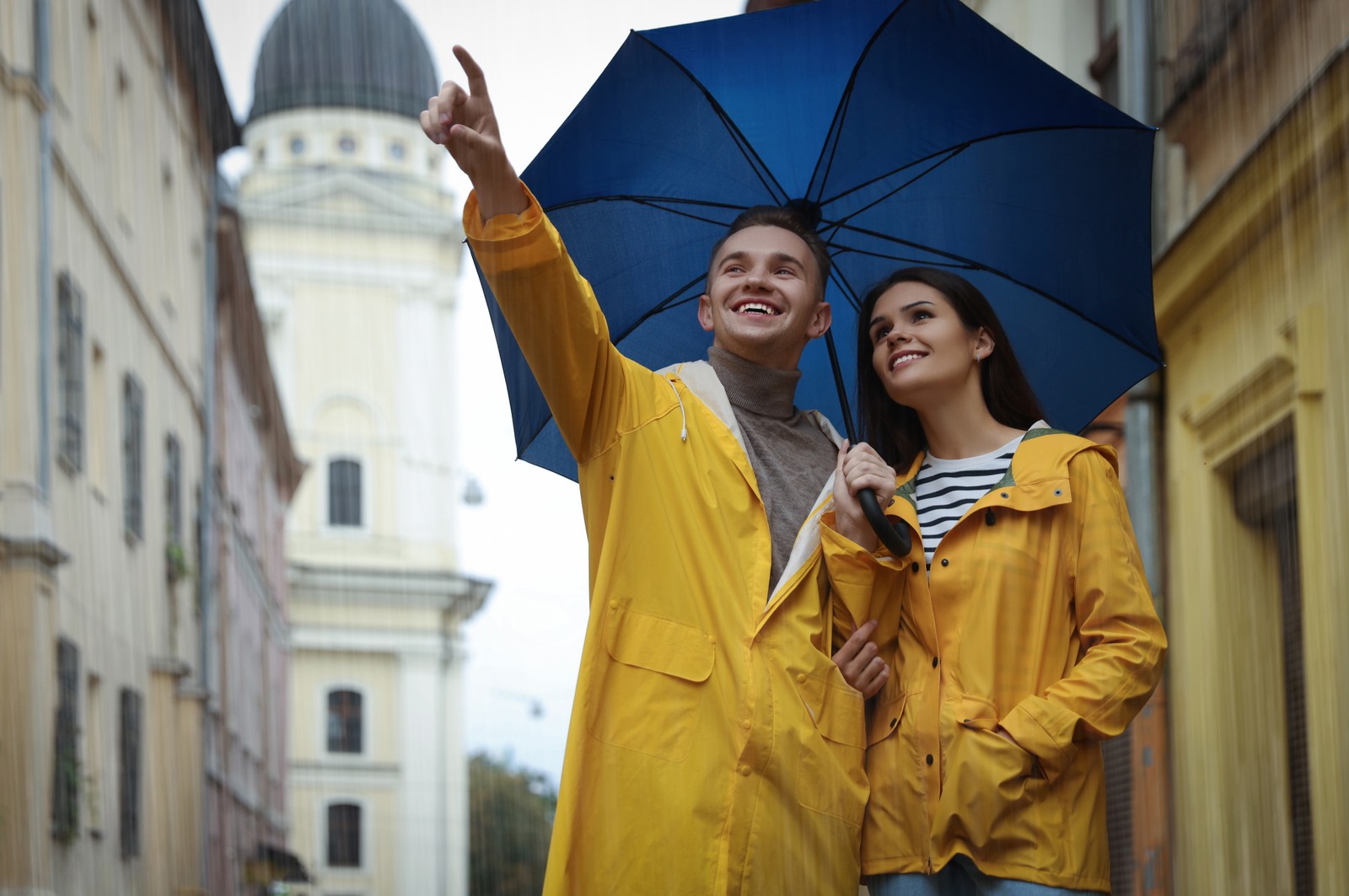 Photo of lovely young couple with umbrella walking under rain on city street