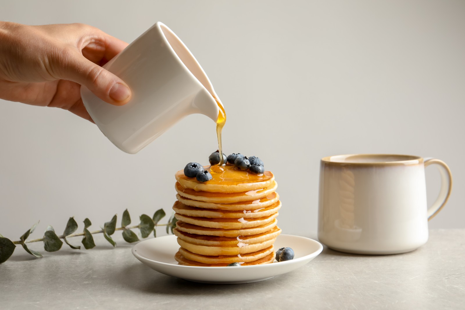 Photo of woman pouring honey onto tasty pancakes with berries on table, closeup