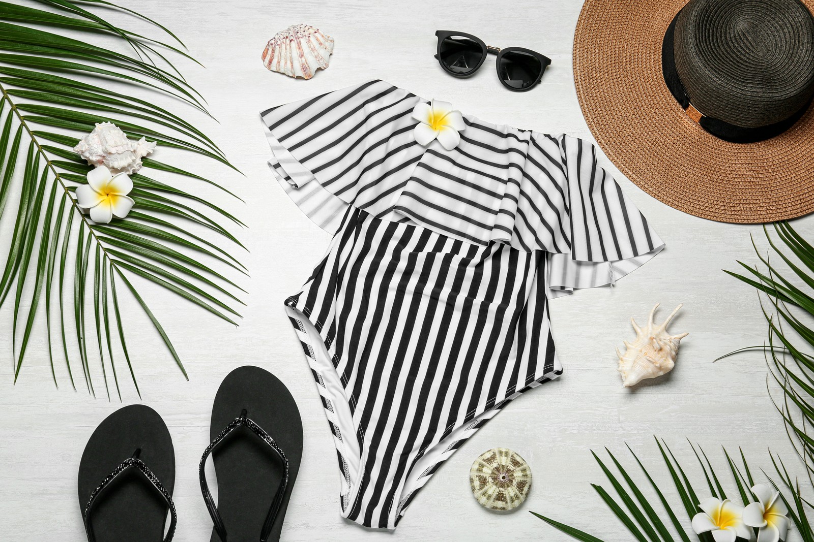 Photo of flat lay composition with striped swimsuit and beach accessories on light stone background