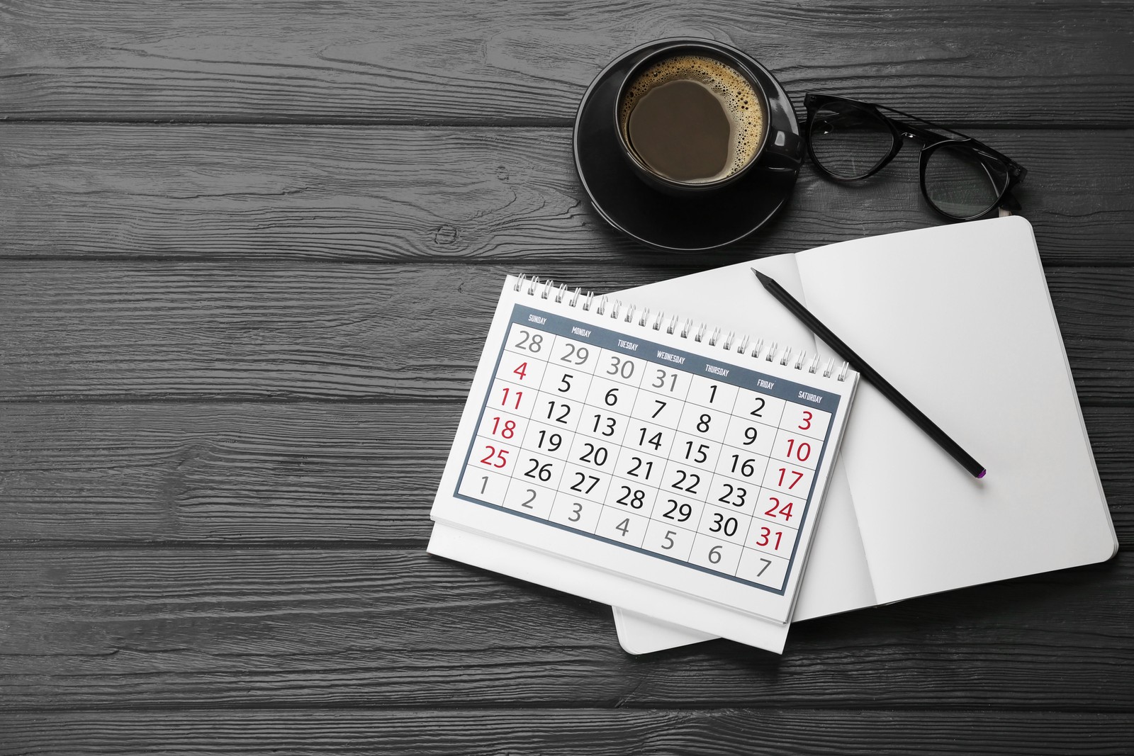 Photo of flat lay composition with calendar and cup of coffee on grey wooden table. Space for text