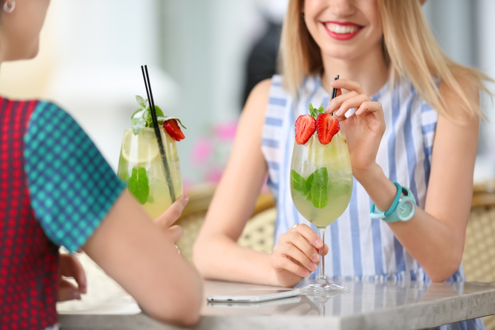 Photo of young women with glasses of tasty lemonade in open-air cafe