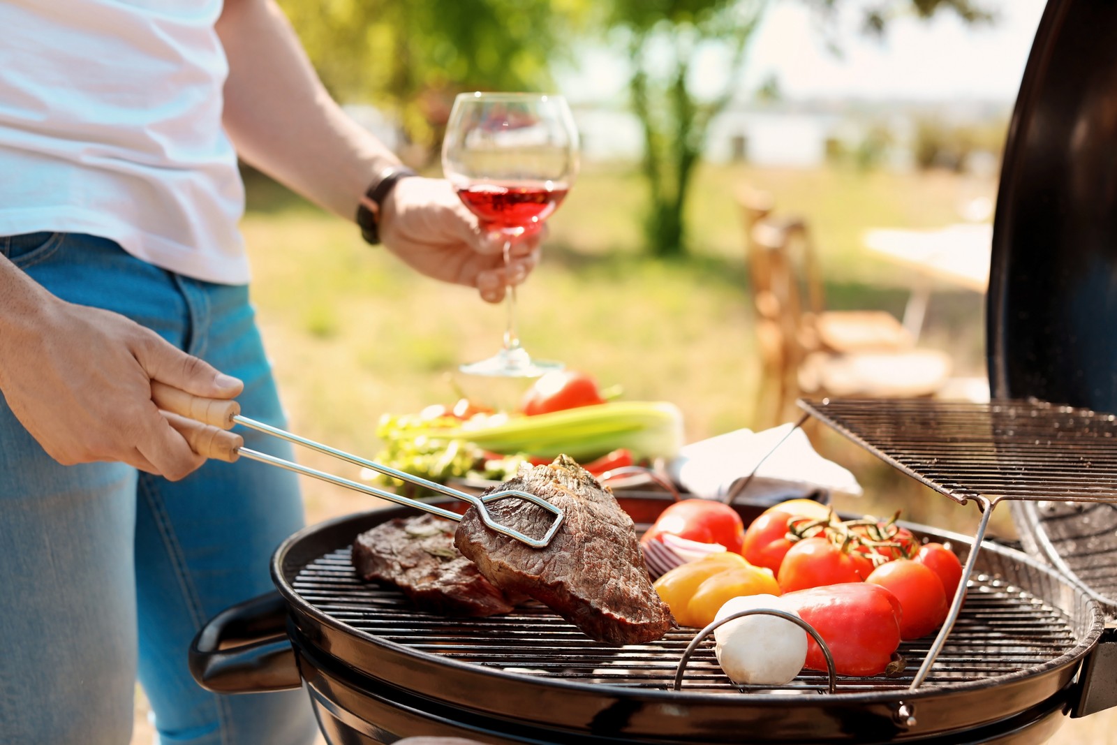 Photo of man cooking meat and vegetables on barbecue grill outdoors