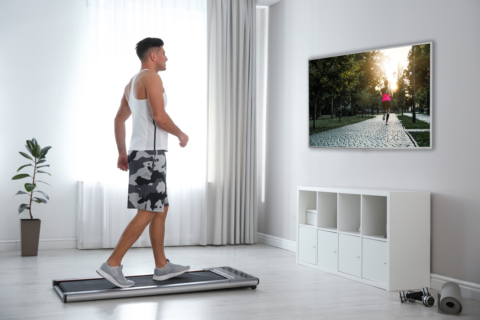 Photo of sporty man training on walking treadmill and watching TV at home