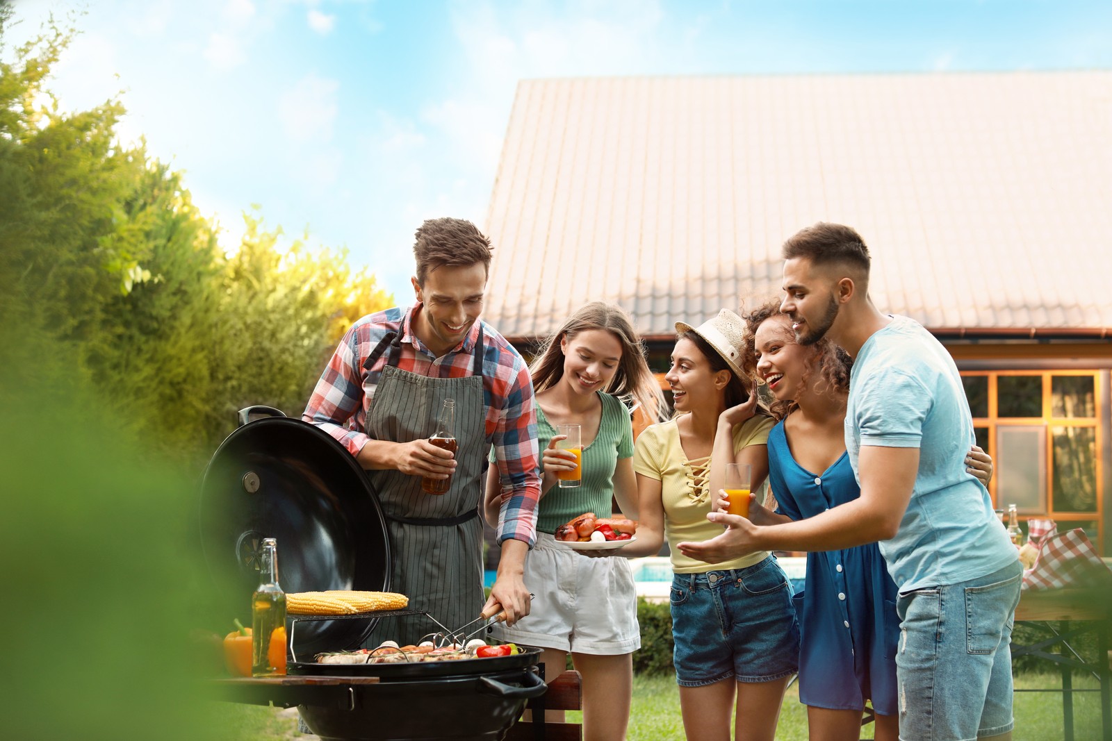 Photo of group of friends with drinks near barbecue grill outdoors