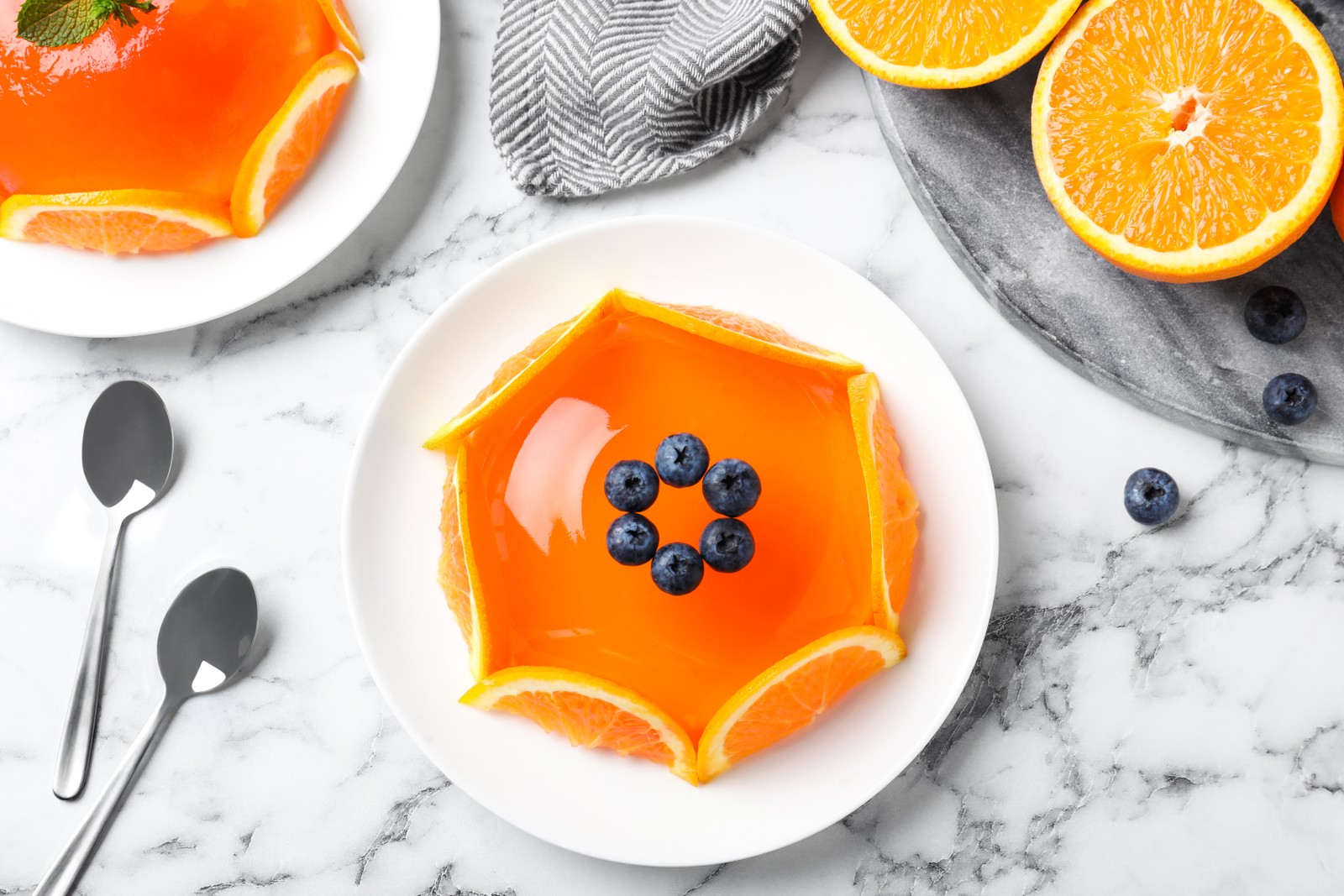 Photo of delicious fresh jelly with orange slices and blueberries on marble table, flat lay