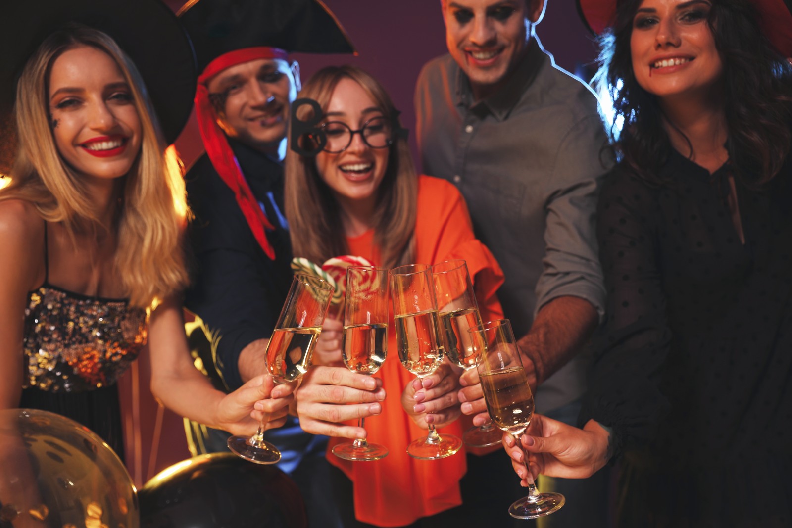 Photo of happy friends in costumes enjoying Halloween party on dark background