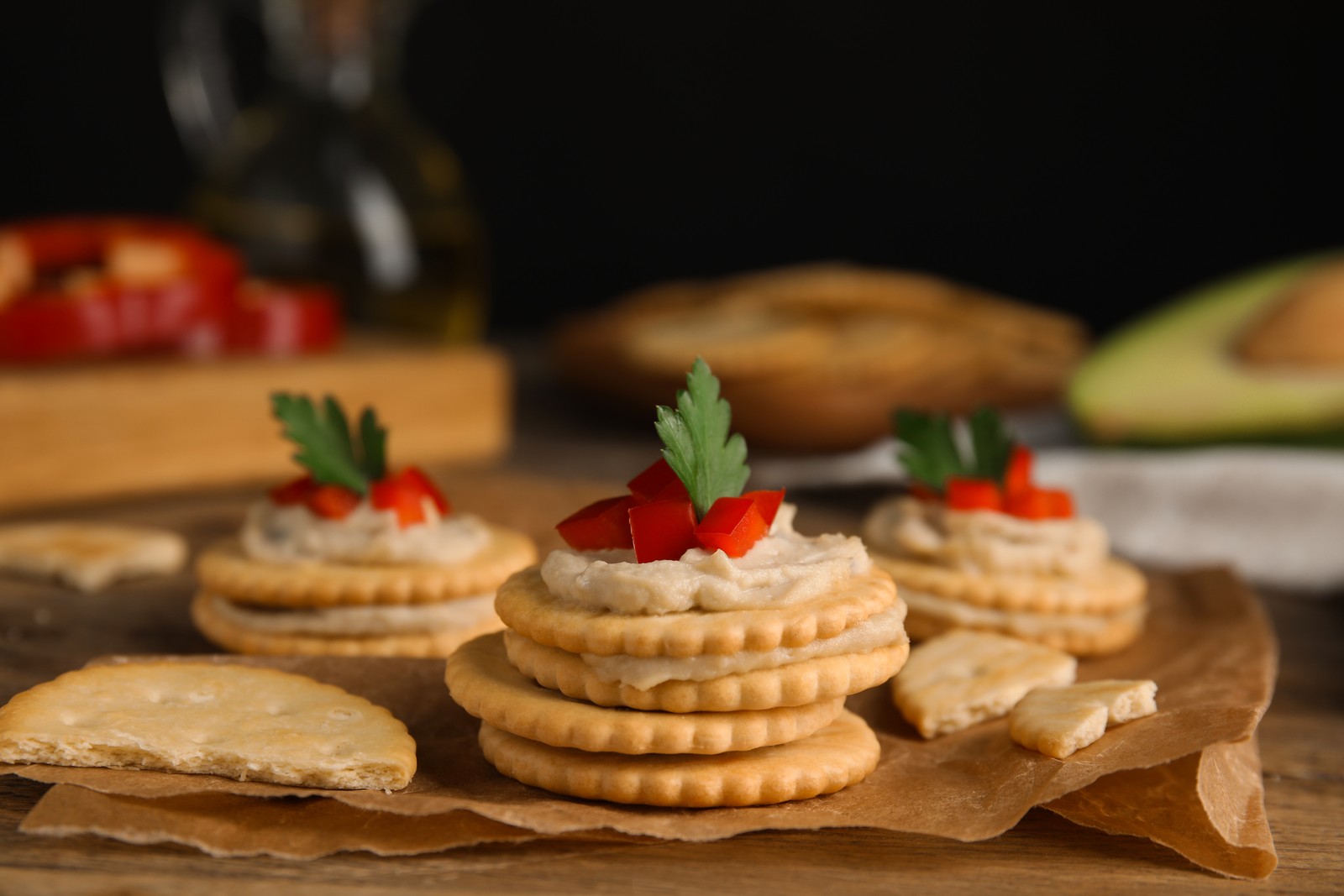 Photo of delicious crackers with humus, bell pepper and parsley on wooden table