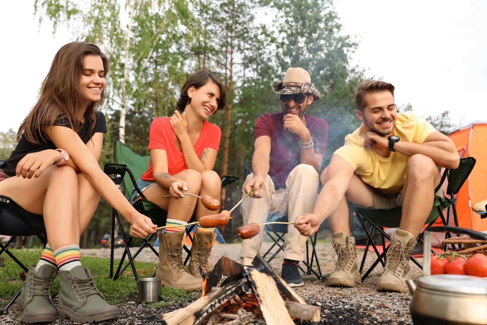 Photo of people having lunch with sausages near camping tent outdoors