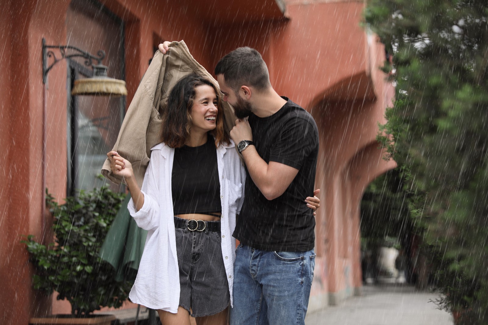 Photo of young couple enjoying time together under rain on city street, space for text