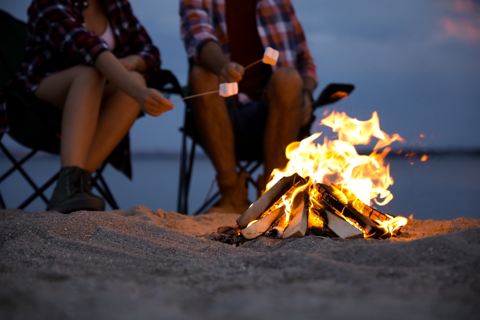 Photo of people roasting marshmallows over burning firewood on beach, closeup