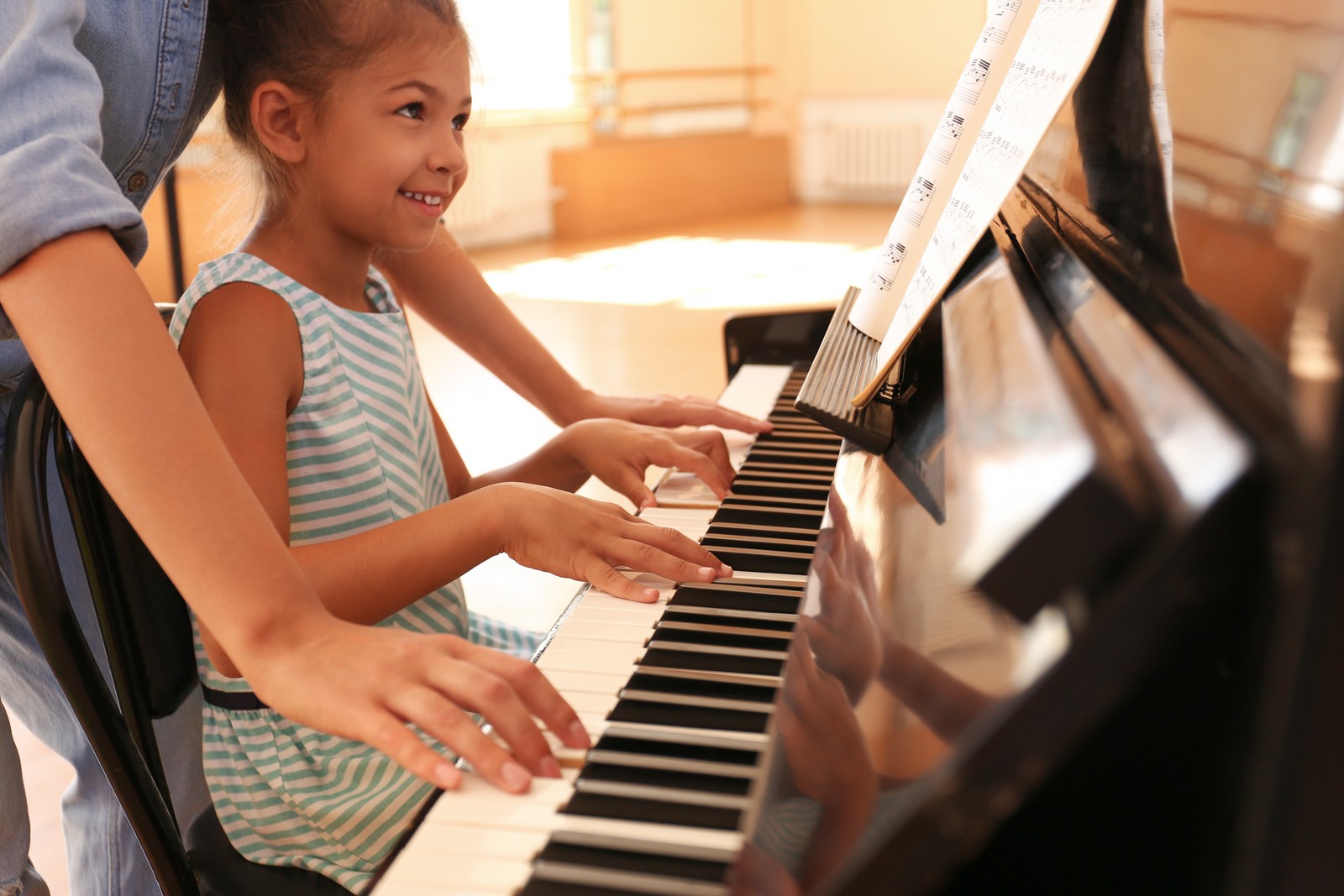 Photo of young woman teaching little girl to play piano indoors