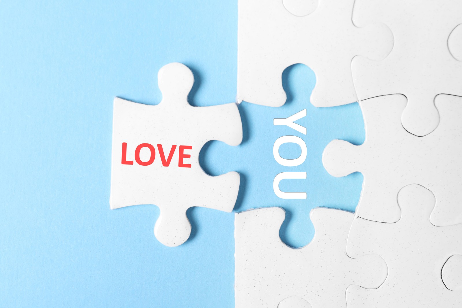 Photo of puzzle with phrase LOVE YOU on light blue background, top view
