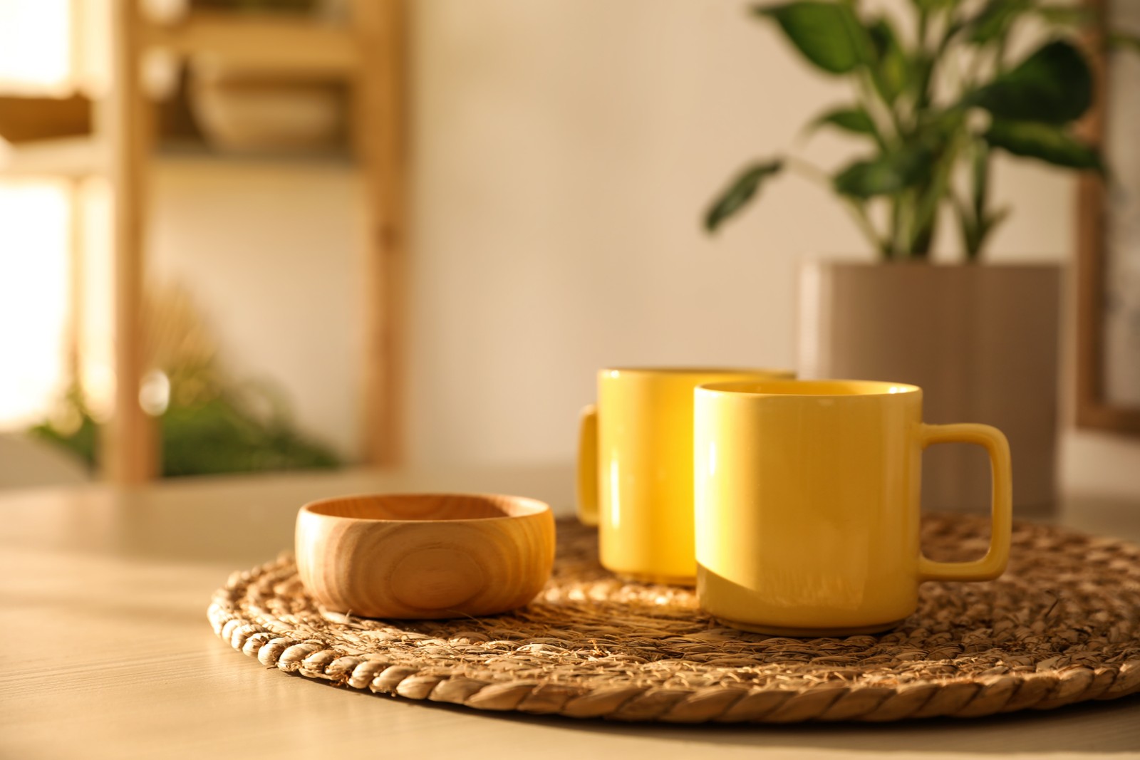 Photo of yellow cups and wooden bowl on wicker mat in kitchen