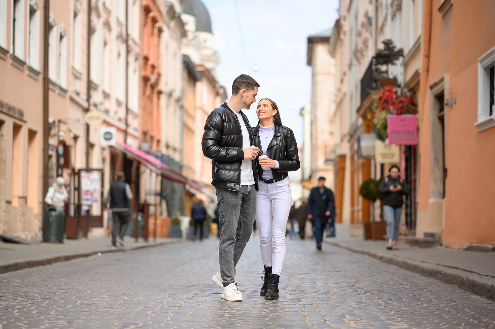 Photo of lovely young couple with cups of coffee walking together on city street. Romantic date