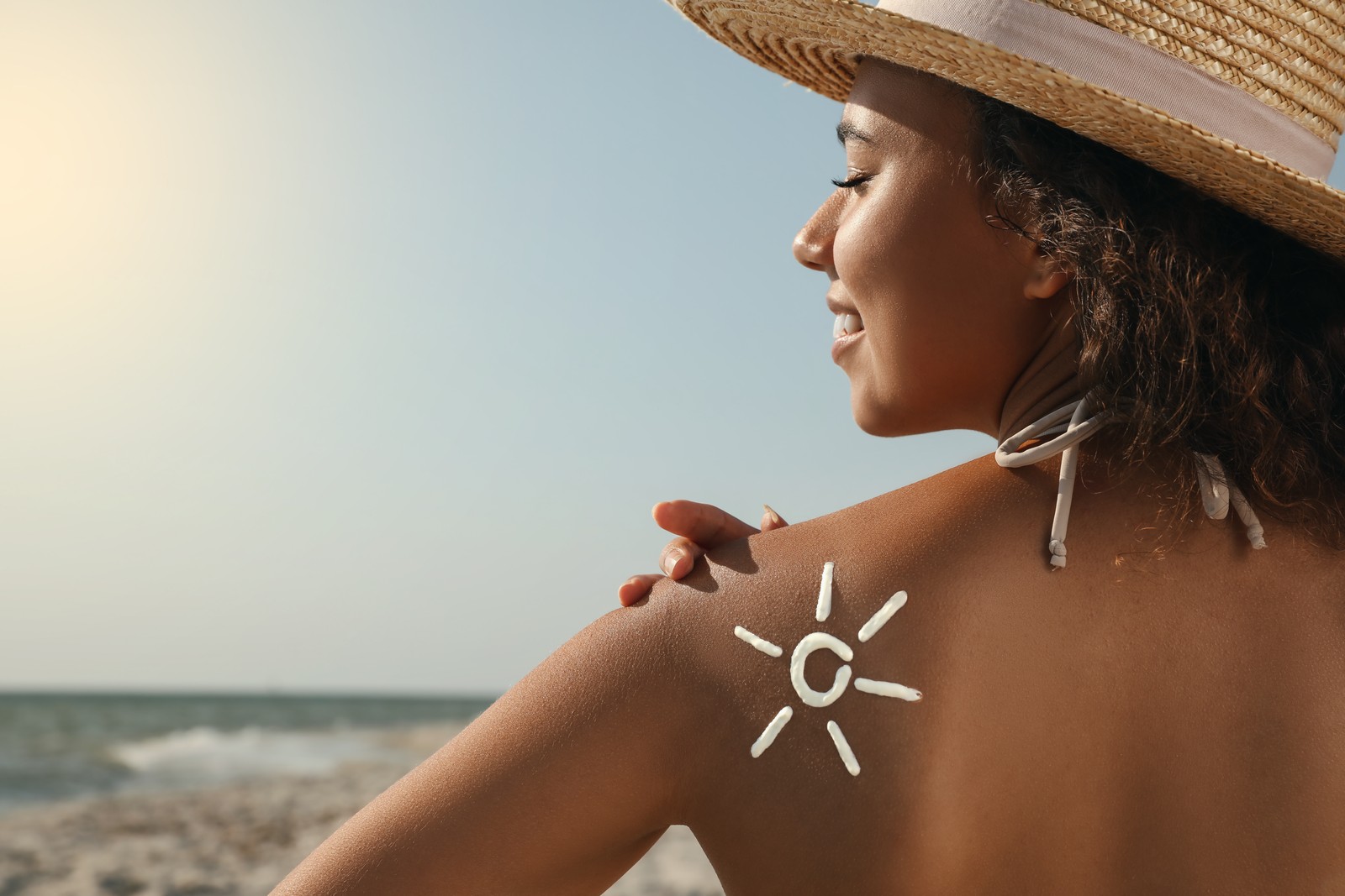 Photo of beautiful African American woman with sun protection cream on shoulder at beach