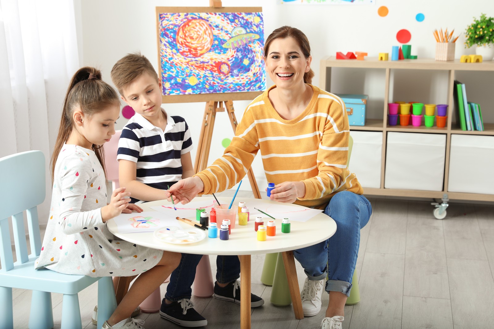 Photo of children with female teacher at painting lesson indoors