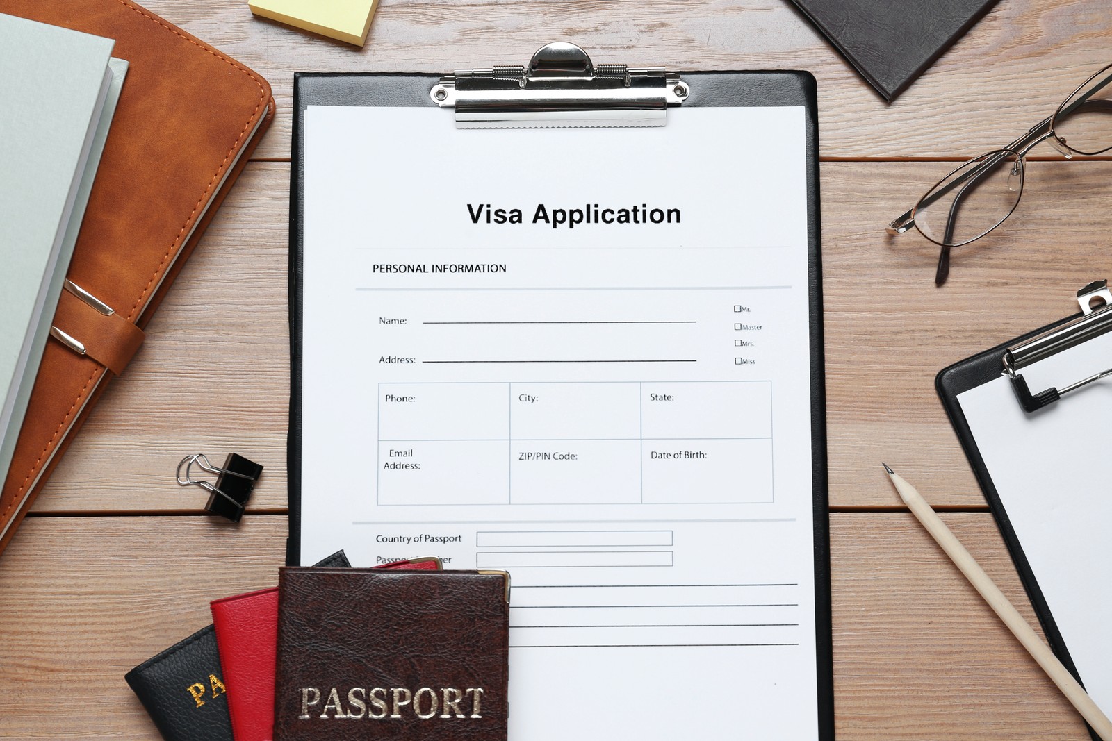 Photo of visa application form for immigration, passports and stationery on wooden table, flat lay