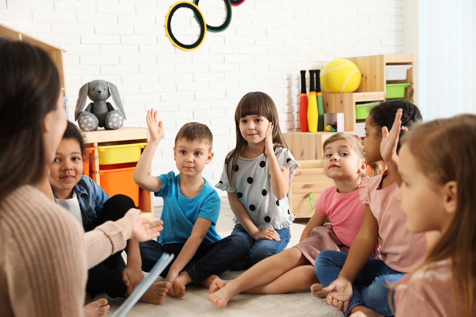 Photo of kindergarten teacher reading book to cute little children indoors