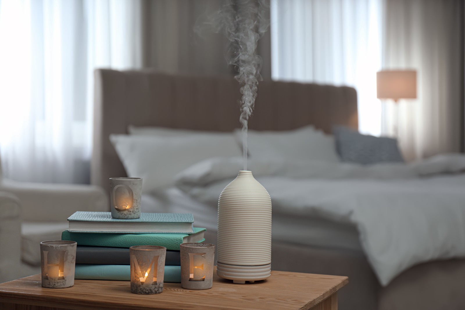 Photo of aroma oil diffuser, candles and books on wooden table in bedroom