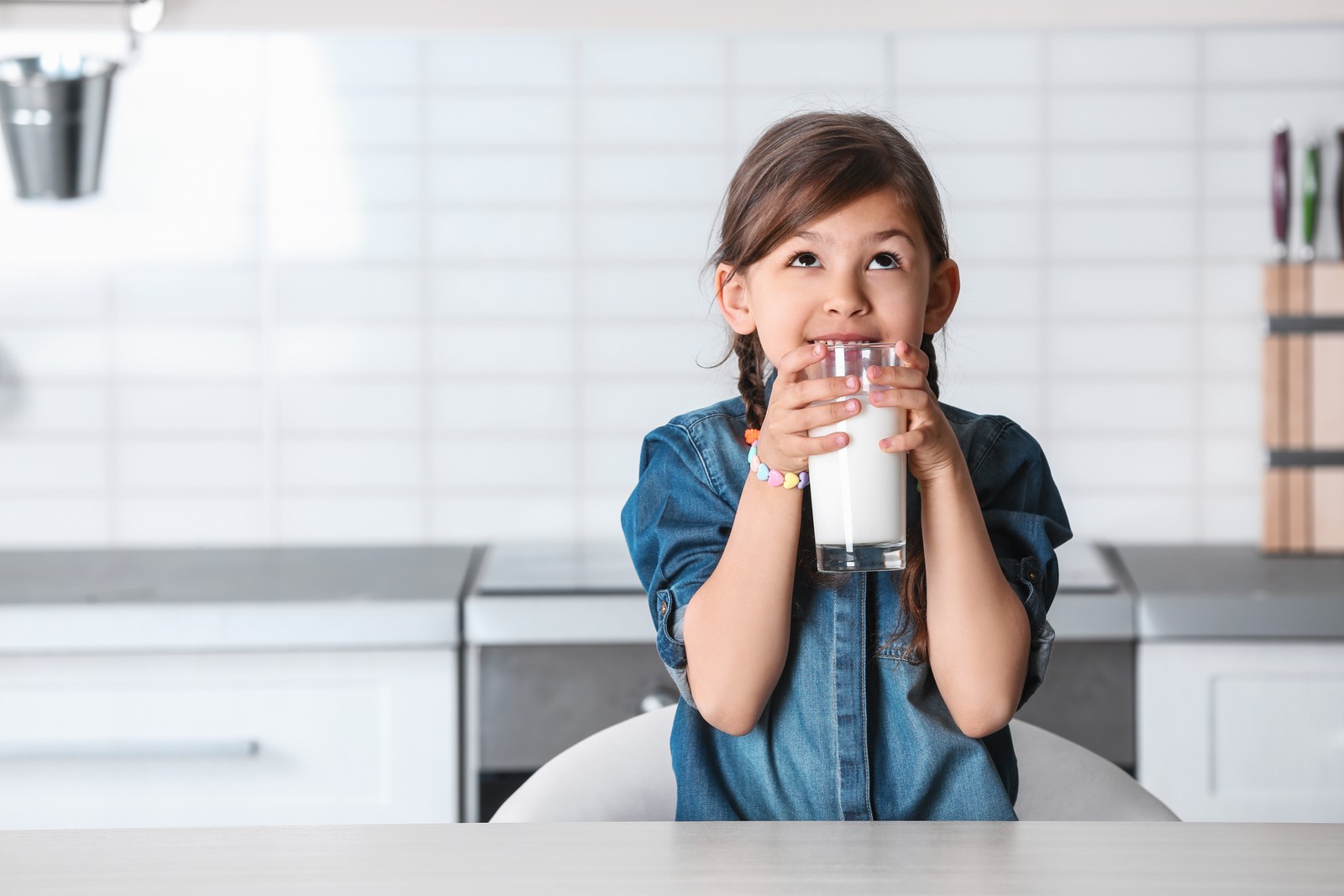 Photo of cute little girl drinking milk at table in kitchen