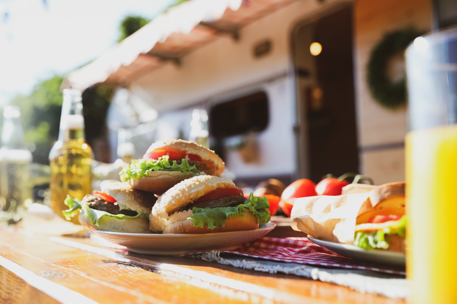 Photo of delicious burgers on wooden table near motorhome. Camping season