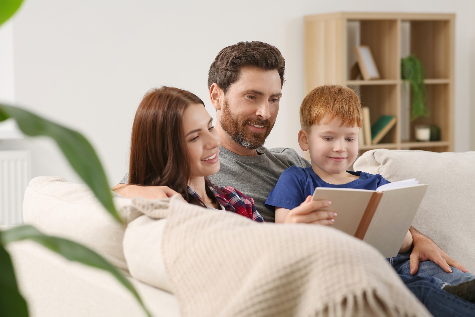 Photo of happy parents with their child reading book on couch at home