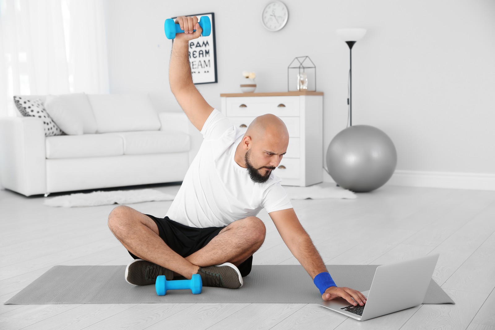 Photo of overweight man doing exercise while watching tutorial on laptop at home