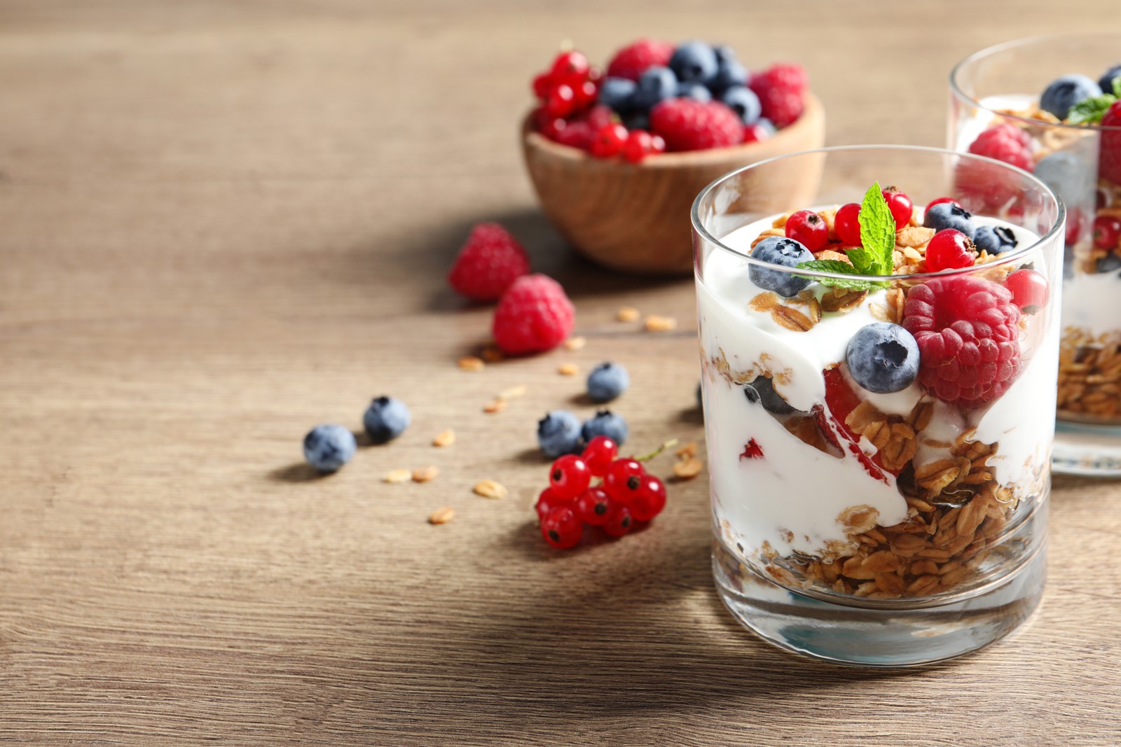 Photo of tasty dessert with yogurt, berries and granola on wooden table. Space for text