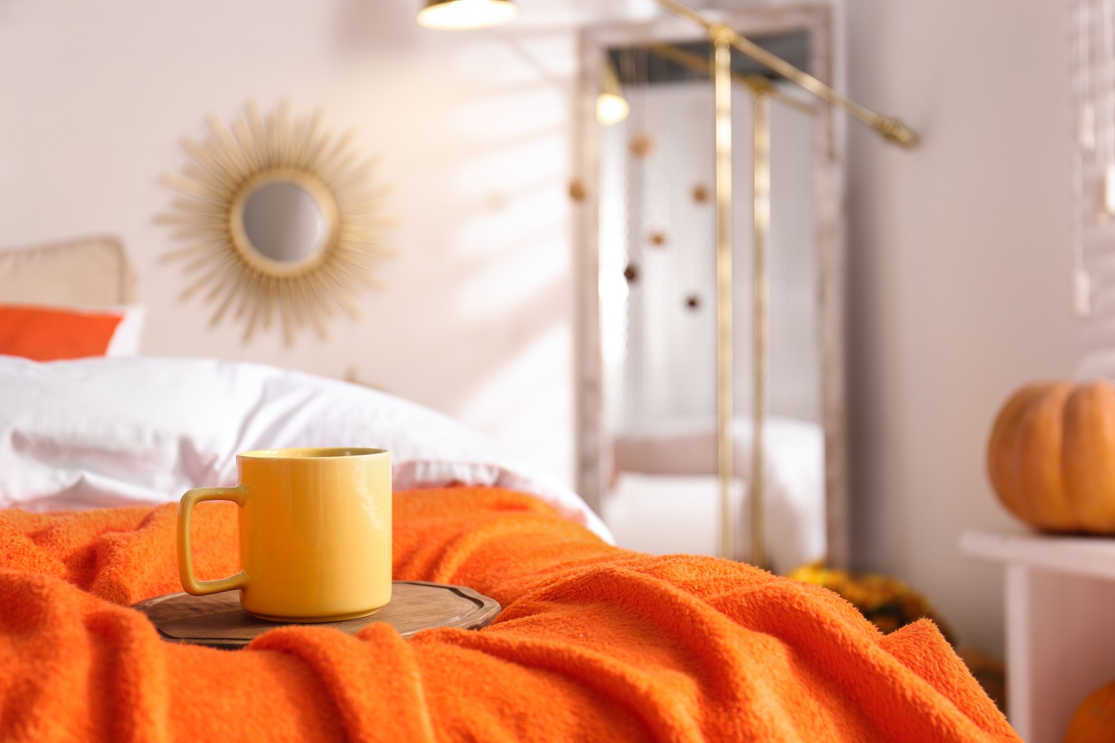 Photo of hot drink on bed with orange blanket at home. Idea for decor in autumn colors