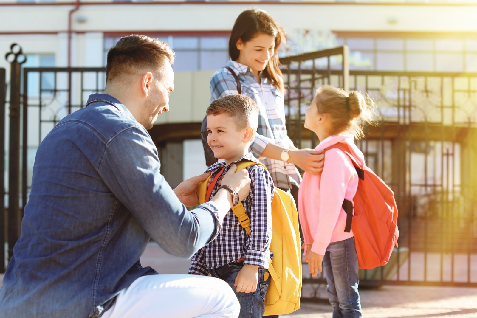 Photo of young parents saying goodbye to their little children near school