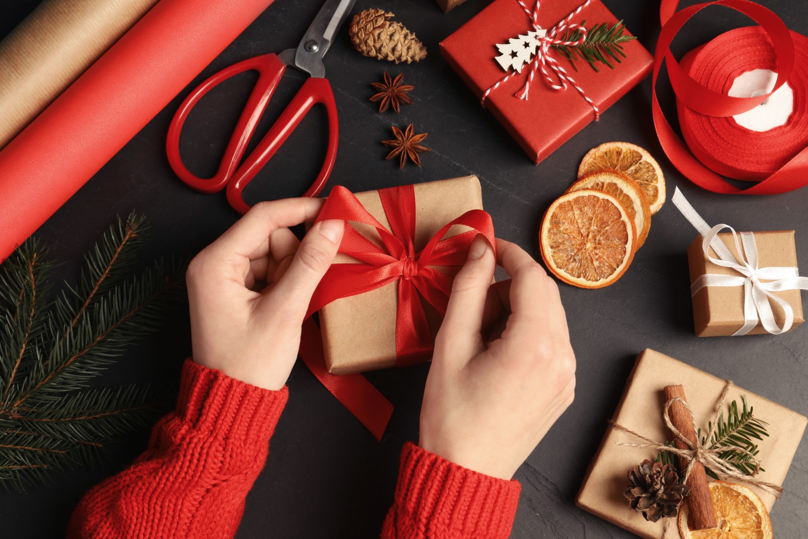 Photo of woman decorating gift box at black table, top view. Christmas present