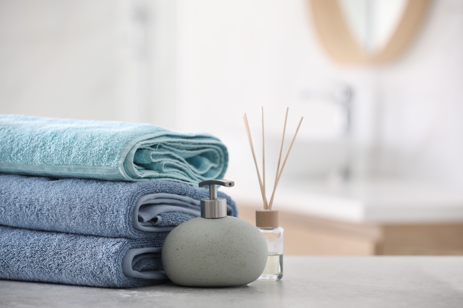 Photo of stack of fresh towels, reed air freshener and soap dispenser on table in bathroom