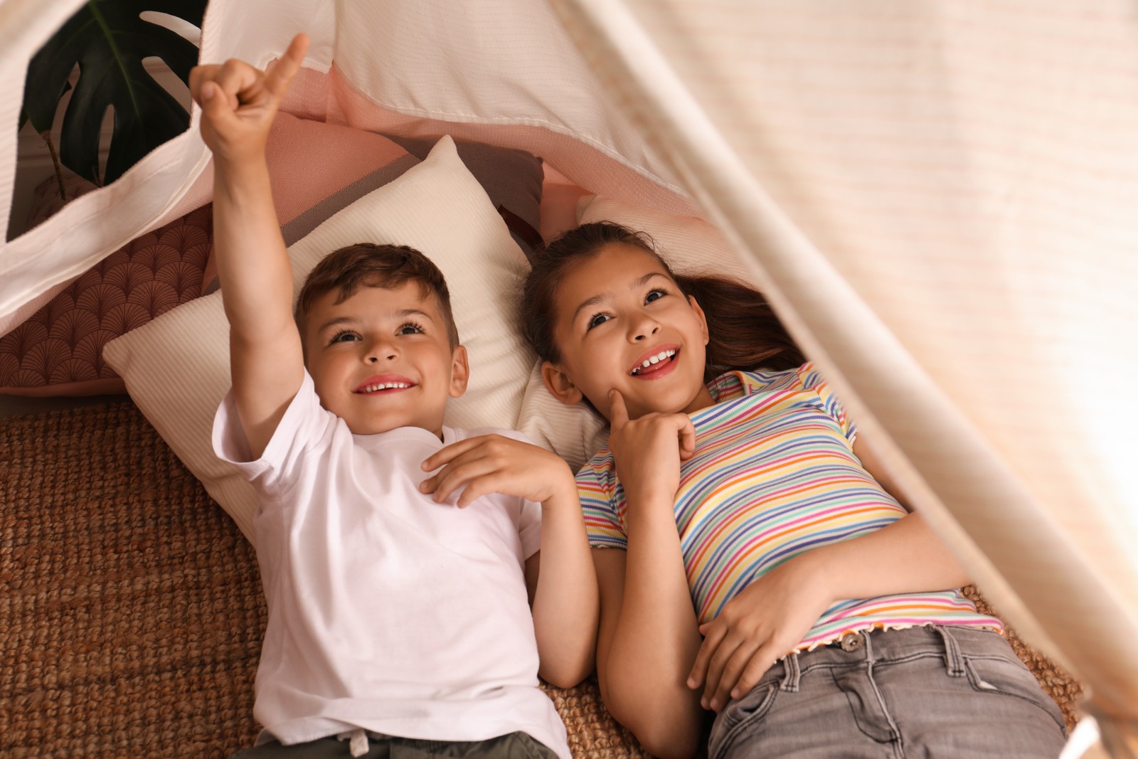 Photo of cute little children lying in toy wigwam at home