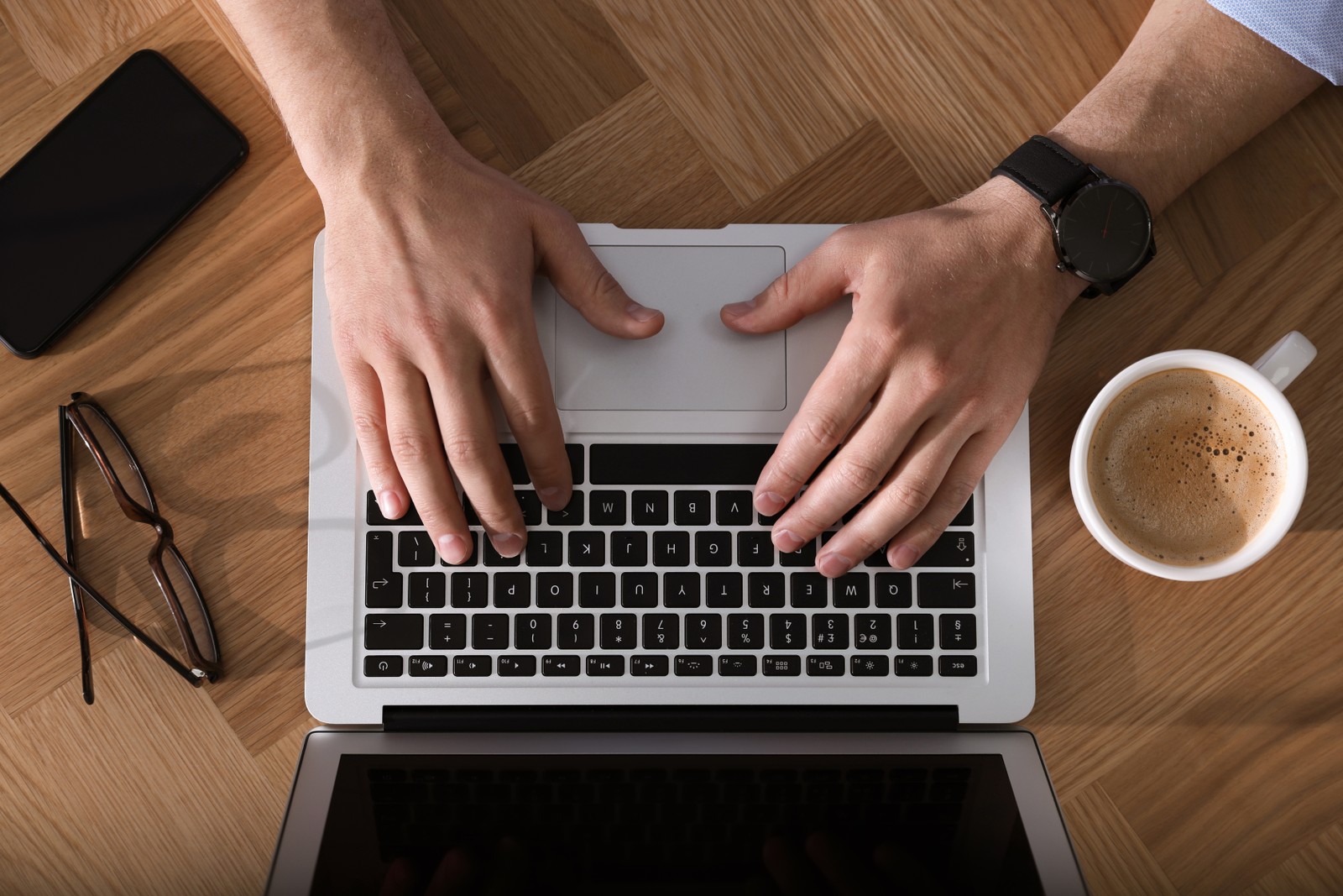 Photo of man with laptop, cup of coffee and smartphone at wooden table, top view