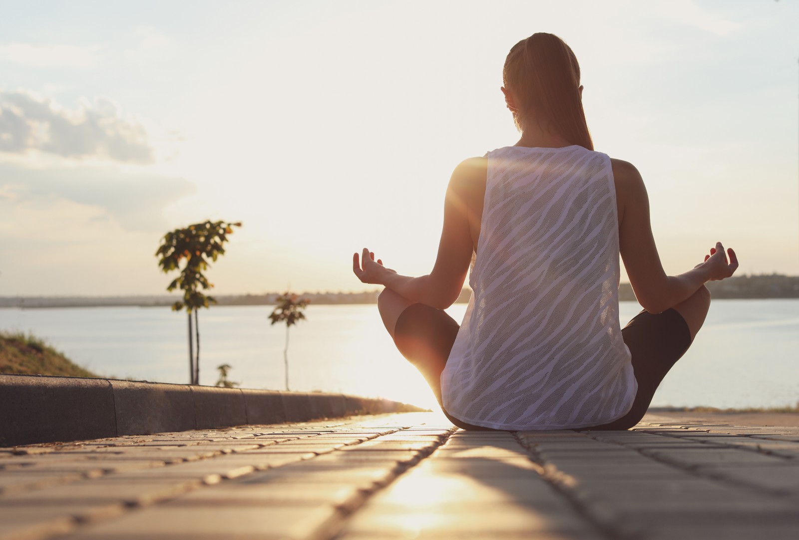 Photo of young woman meditating near river in morning, back view. Space for text