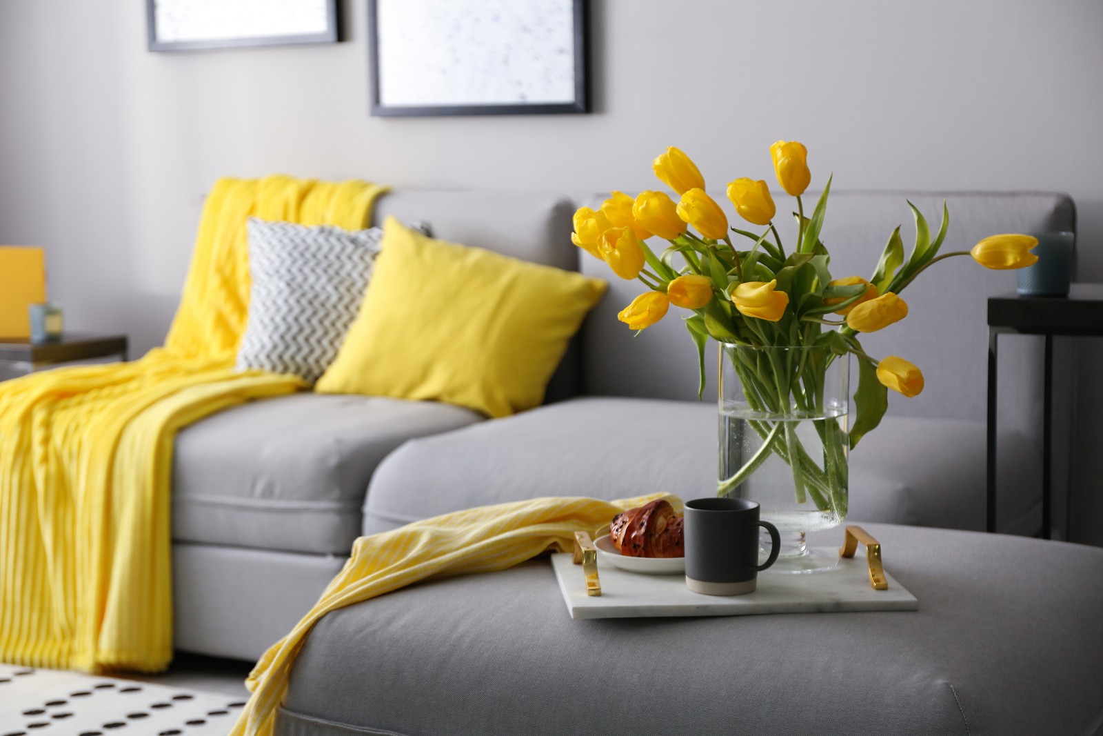 Photo of tray with beautiful tulips on sofa indoors. Interior design in grey and yellow colors