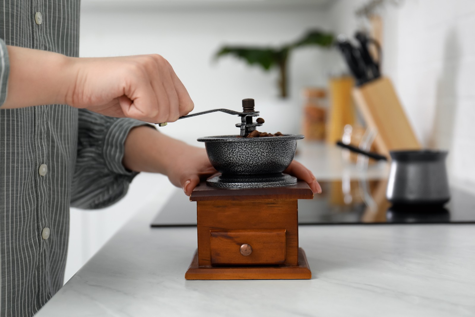Photo of woman using vintage coffee grinder at countertop indoors, closeup